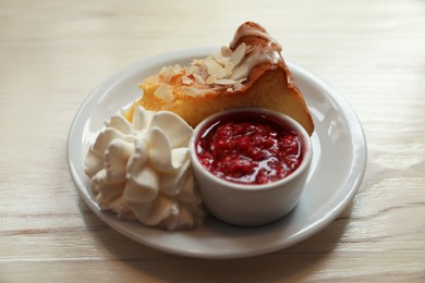 Photo of Piece of delicious cake with whipped cream and jam on white wooden table, closeup