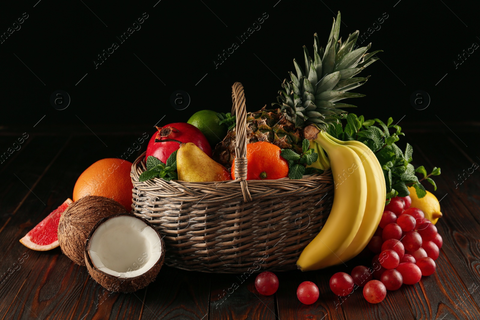Photo of Wicker basket and different ripe fruits on wooden table against black background