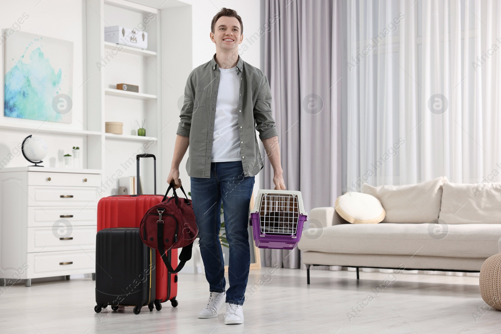 Photo of Travel with pet. Man holding carrier with cute cat and bag at home, space for text
