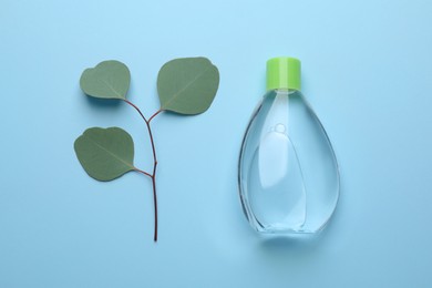 Photo of Bottle of baby oil and eucalyptus leaves on light blue background, flat lay