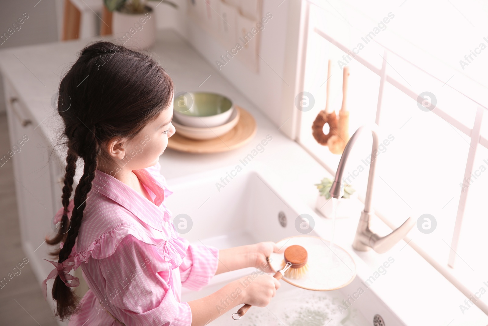 Photo of Little girl washing dishes in kitchen at home