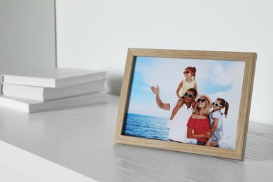 Photo of Frame with family photo and books on white wooden table indoors