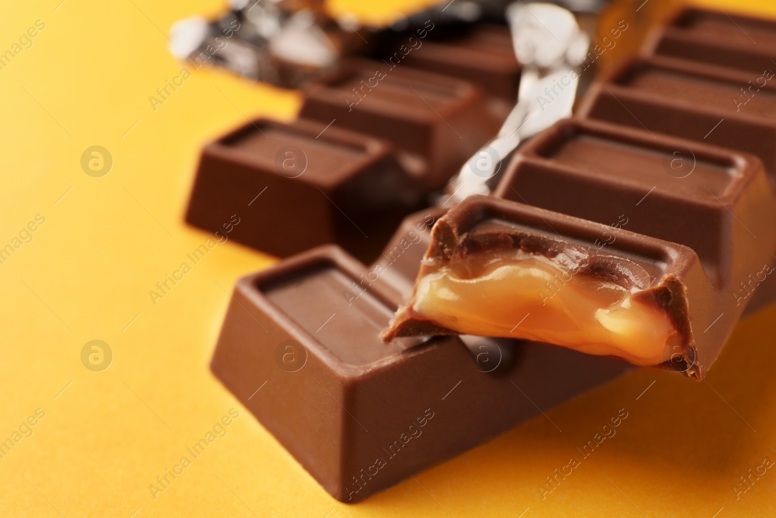 Photo of Tasty chocolate bars on yellow background, closeup. Space for text