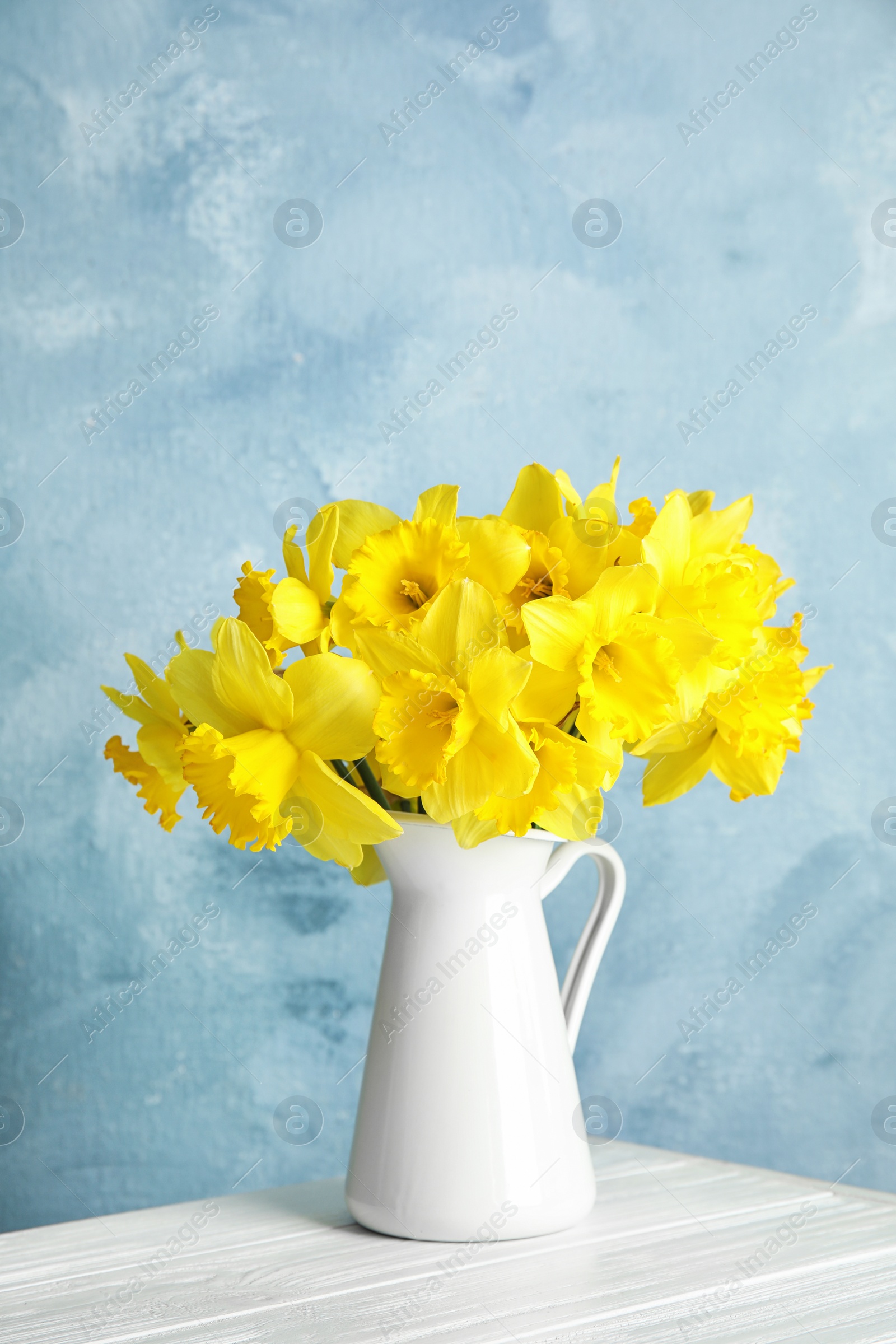 Photo of Bouquet of daffodils in jug on table against color background, space for text. Fresh spring flowers