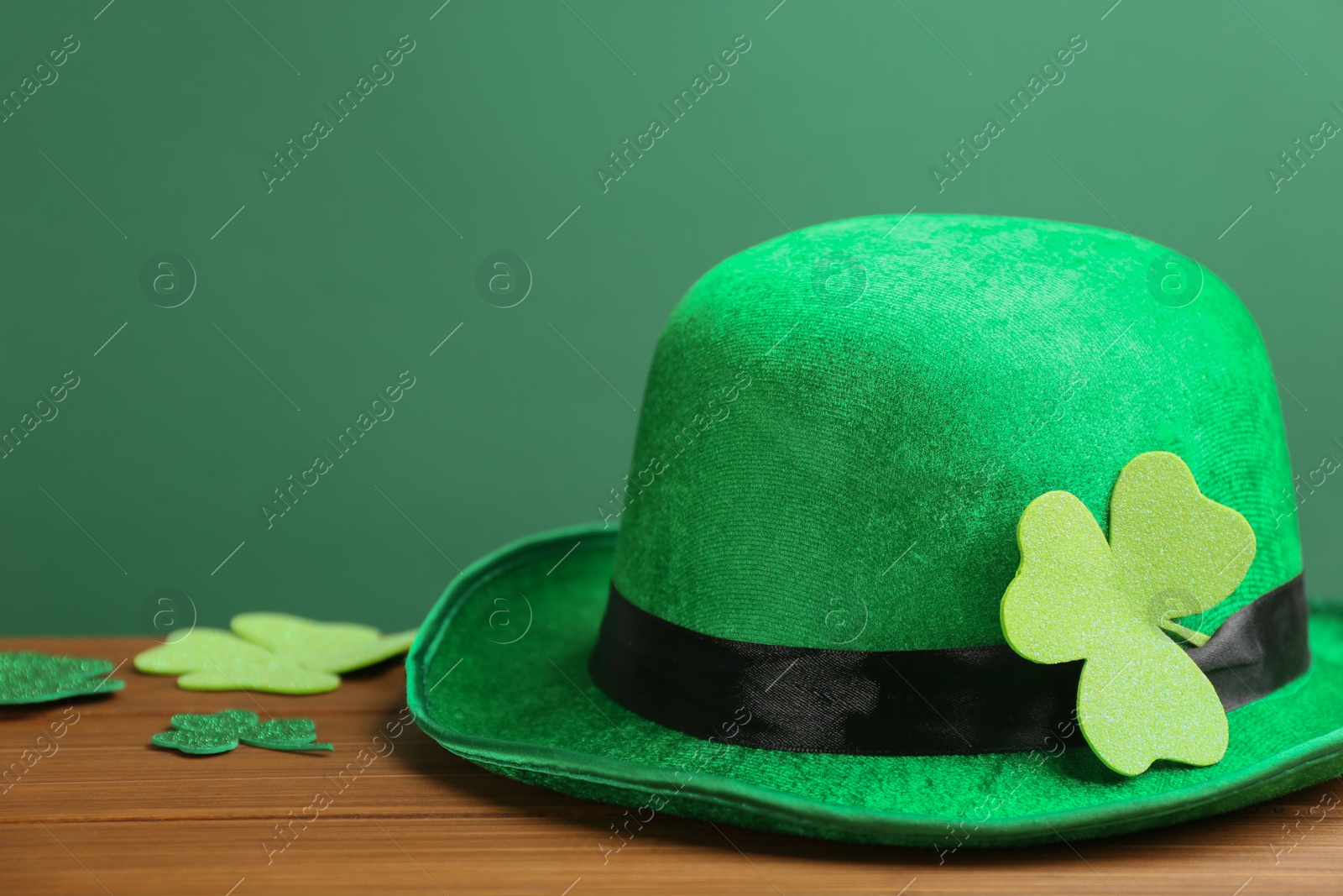 Photo of Leprechaun hat and decorative clover leaves on wooden table against green background, space for text. St Patrick's Day celebration