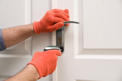 Photo of Handyman with screw gun repairing door lock, closeup