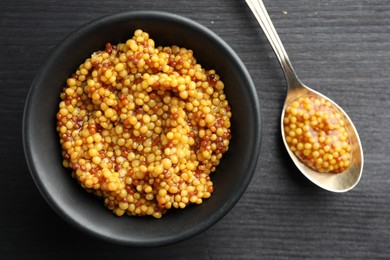 Photo of Bowl and spoon with whole grain mustard on black wooden table, top view