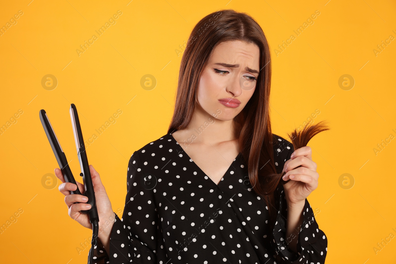 Photo of Upset young woman with flattening iron on yellow background. Hair damage