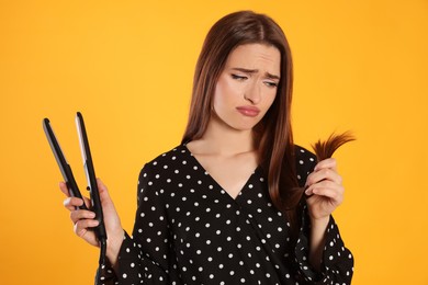 Photo of Upset young woman with flattening iron on yellow background. Hair damage