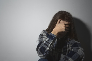 Photo of Abused young woman crying near white wall, space for text. Domestic violence concept