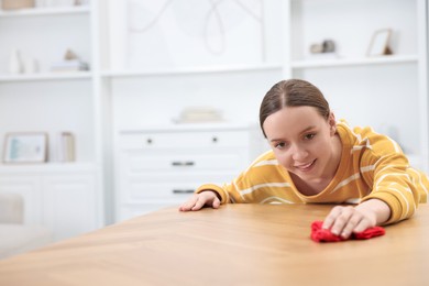 Photo of Woman cleaning wooden table with rag indoors, space for text