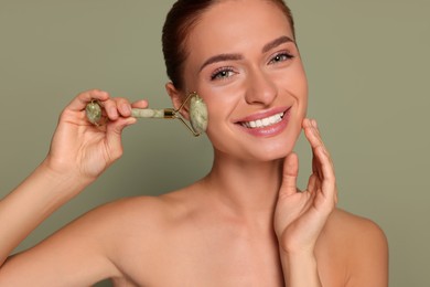 Photo of Young woman massaging her face with jade roller on green background