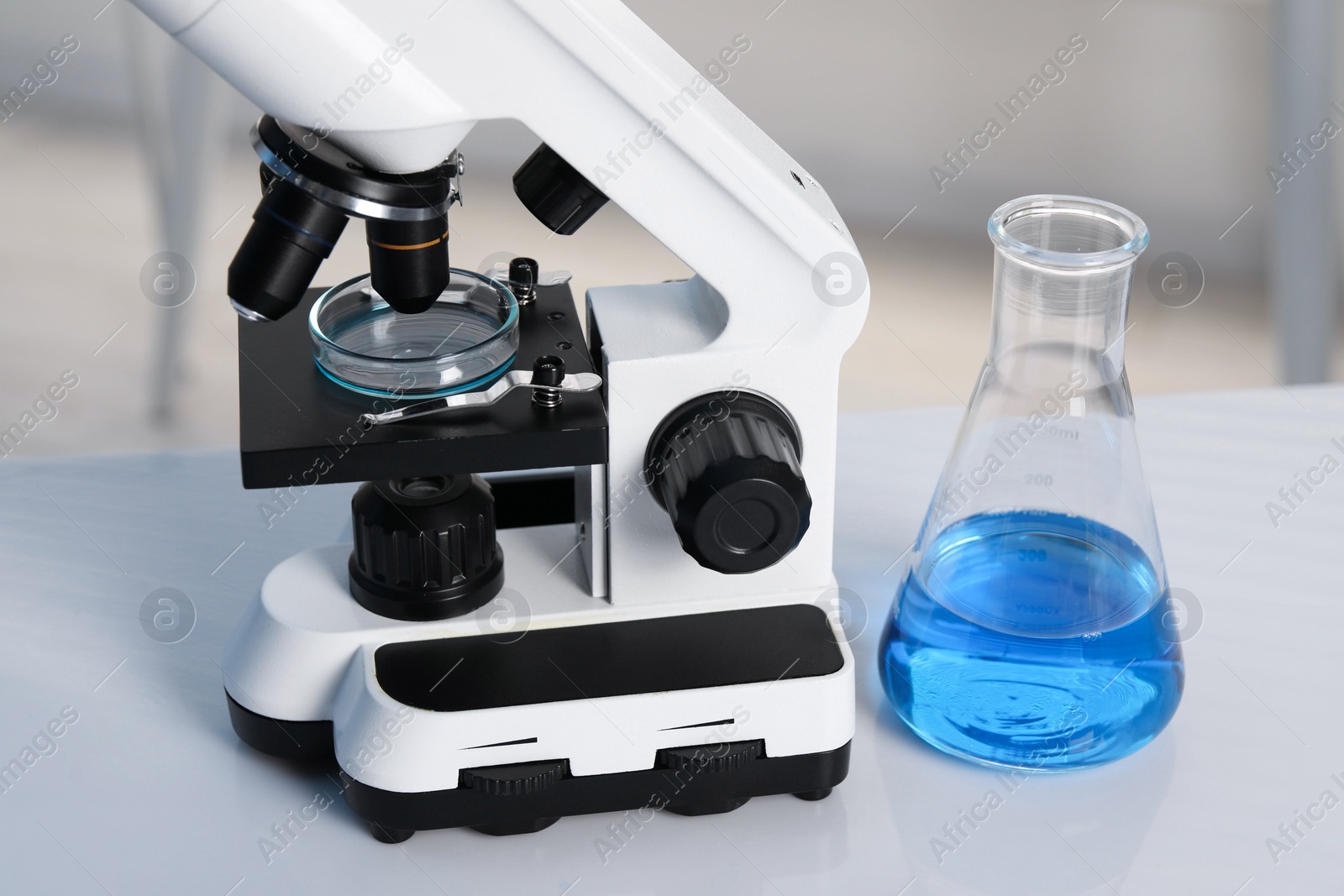 Photo of Laboratory analysis. Flask with blue liquid, petri dish and microscope on white table indoors