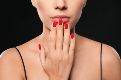 Photo of Beautiful young woman with bright manicure on black background, closeup. Nail polish trends