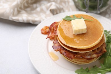 Photo of Delicious pancakes with bacon, butter and arugula on light table, closeup. Space for text