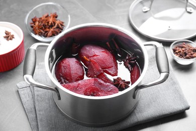 Photo of Tasty red wine poached pears and spices in pot on grey table