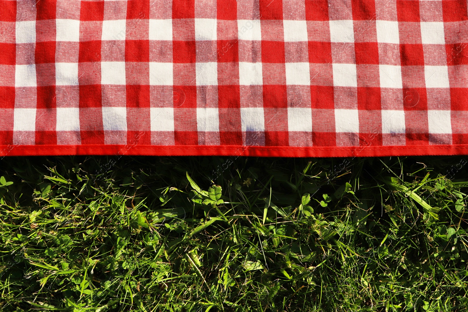 Photo of Checkered picnic tablecloth on fresh green grass, top view. Space for text