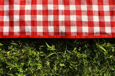 Photo of Checkered picnic tablecloth on fresh green grass, top view. Space for text