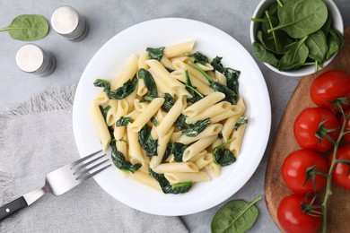 Photo of Tasty pasta with spinach and sauce served on grey textured table, flat lay