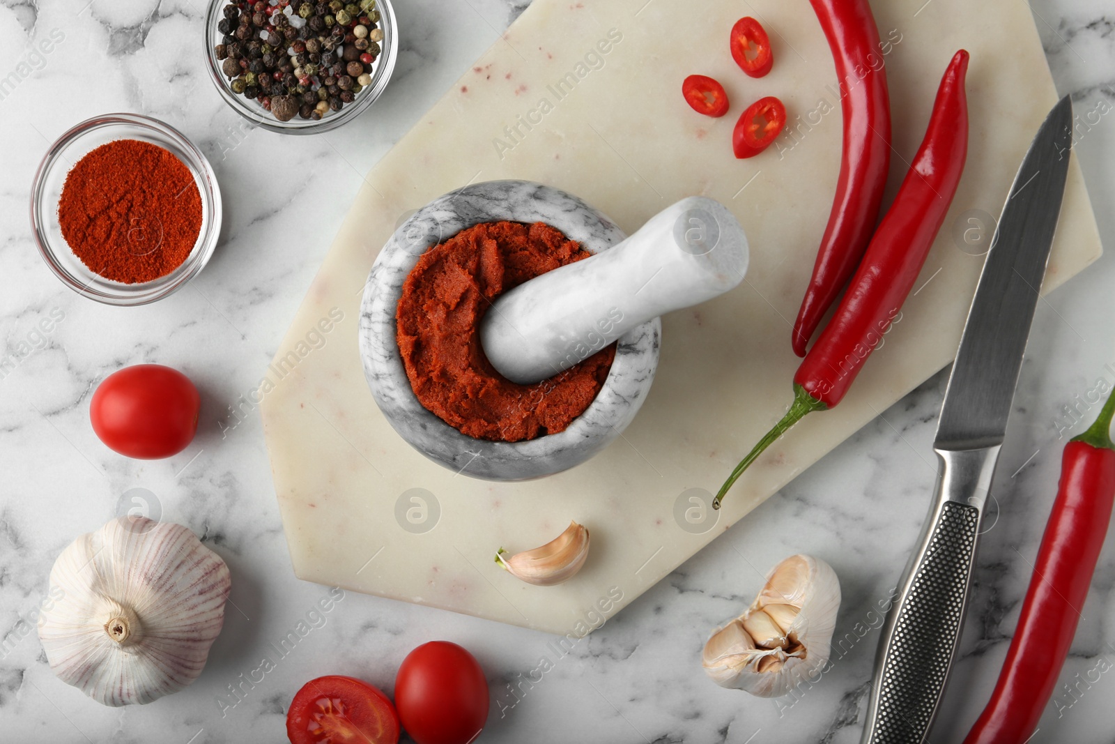 Photo of Red curry paste in mortar and ingredients on white marble table, flat lay