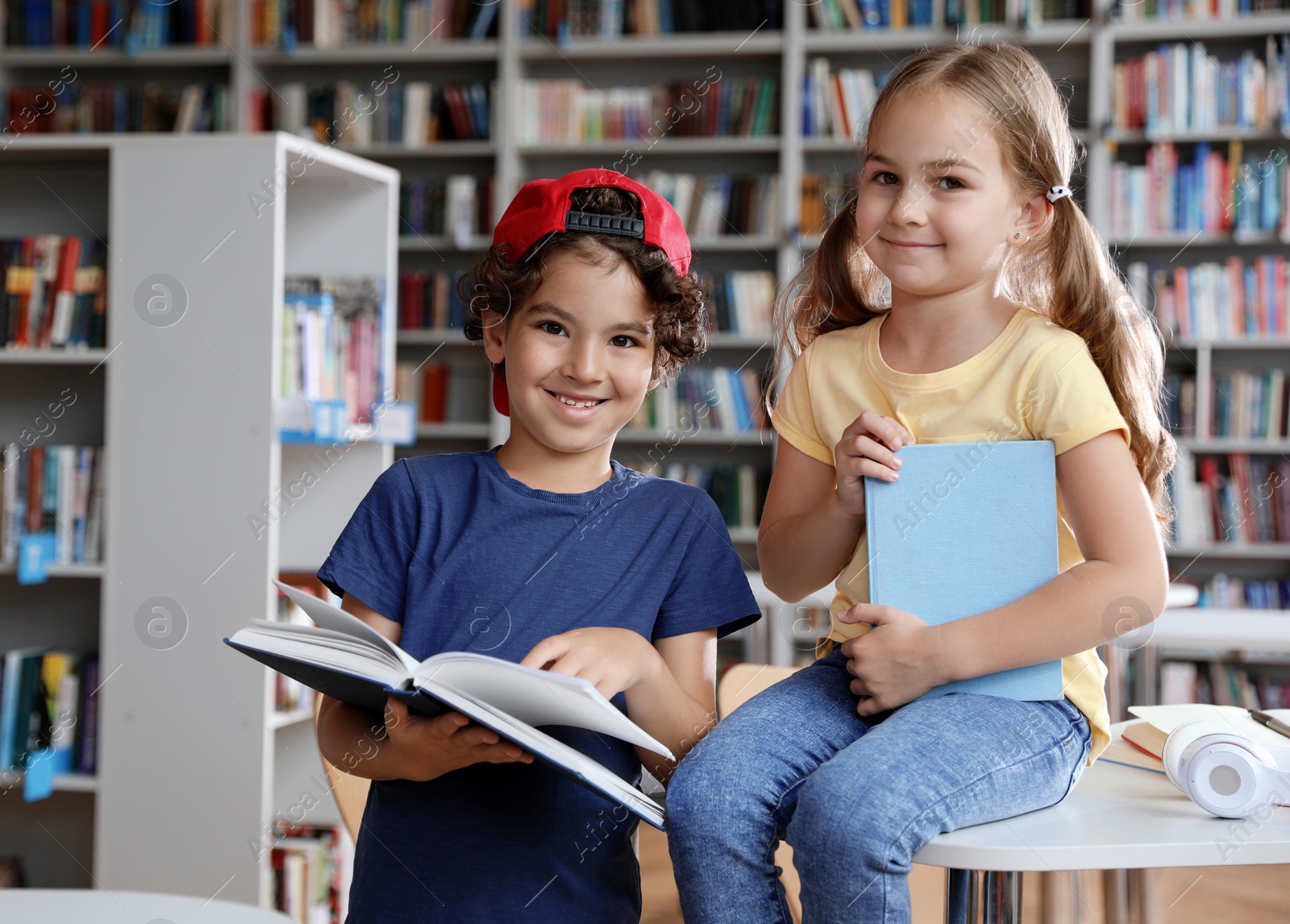 Photo of Little boy and girl reading book in library