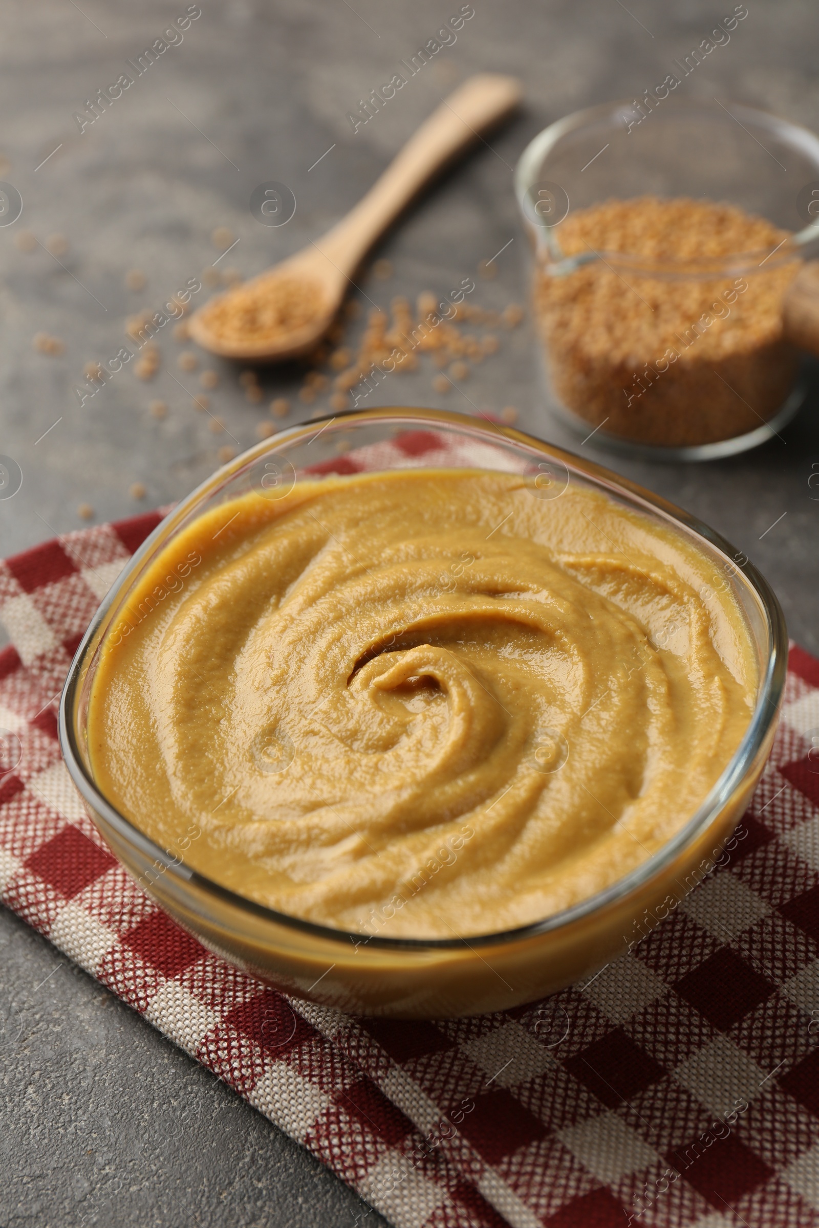 Photo of Tasty mustard sauce in glass bowl on grey table