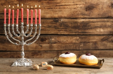 Photo of Silver menorah near sufganiyot and dreidels with symbols Nun, He, Pe, Gimel on wooden background, space for text