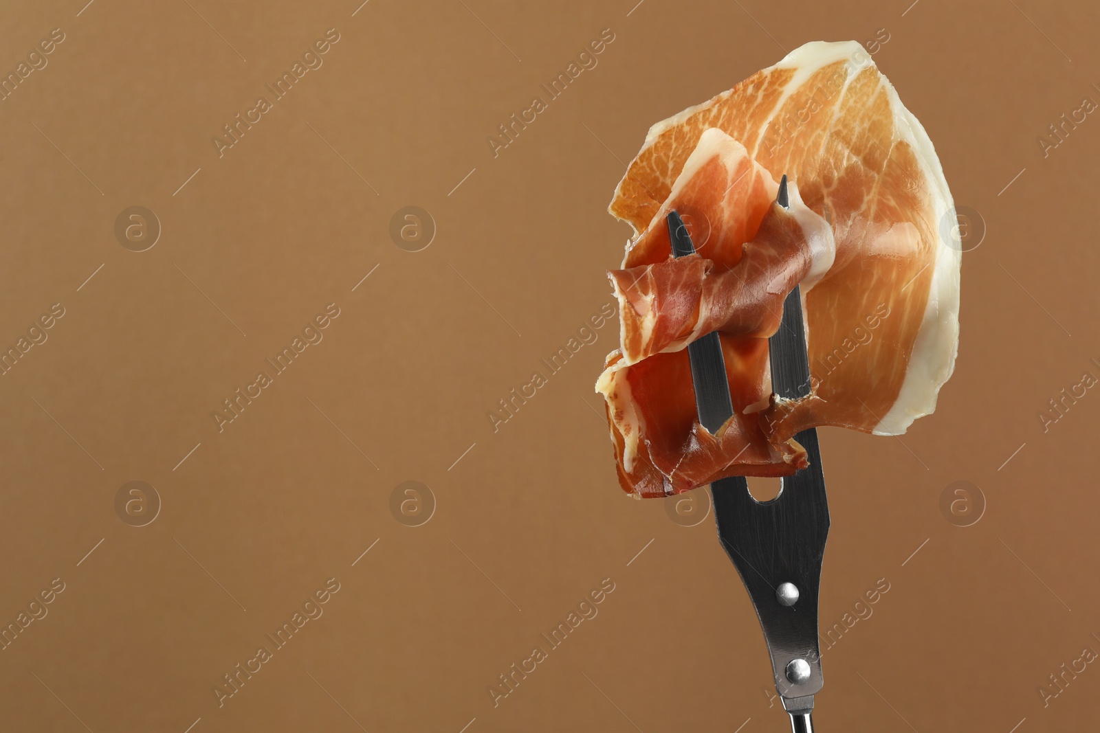 Photo of Fork with slice of tasty jamon on brown background, closeup. Space for text