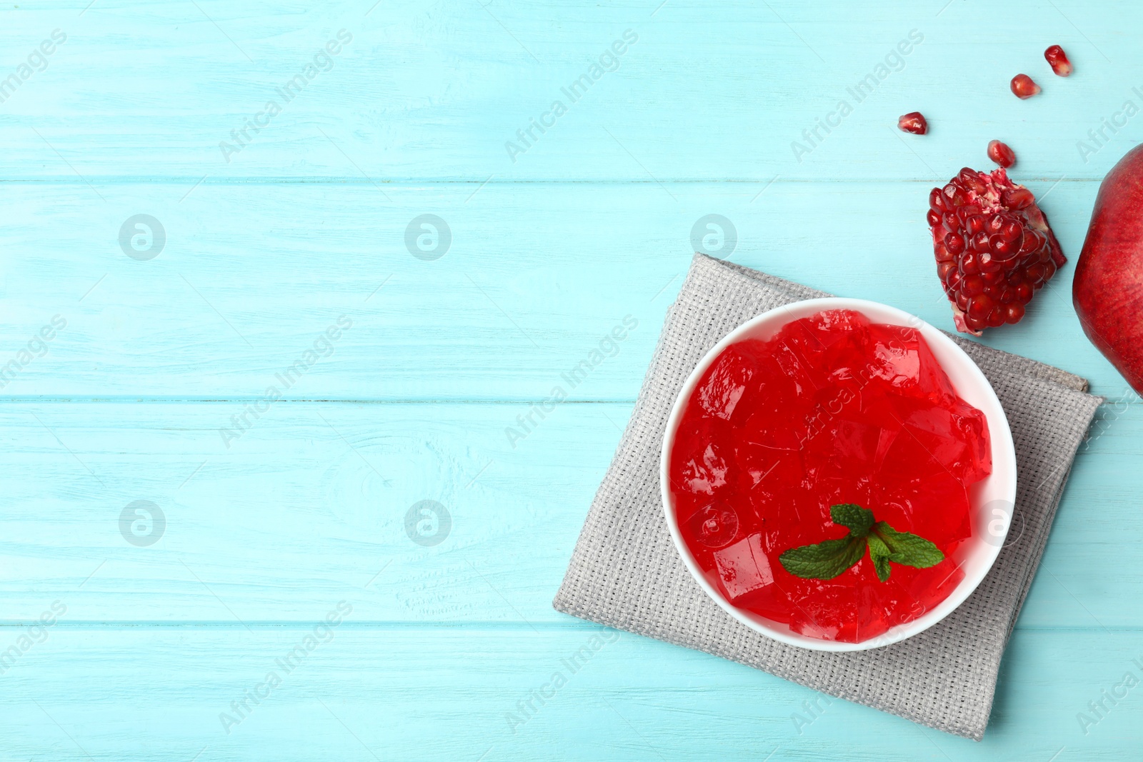 Photo of Flat lay composition with red jelly in bowl and pomegranate on wooden background. Space for text