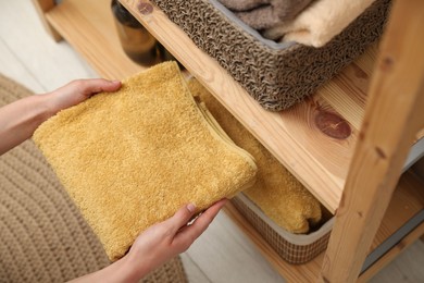 Photo of Woman putting towel into storage basket indoors, closeup