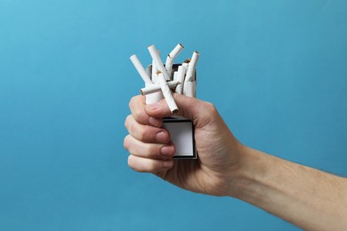 Photo of Stop smoking. Man holding pack with broken cigarettes on light blue background, closeup