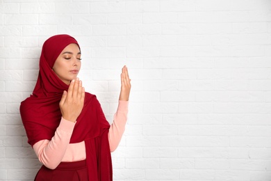 Photo of Portrait of young Muslim woman in hijab praying against brick wall. Space for text