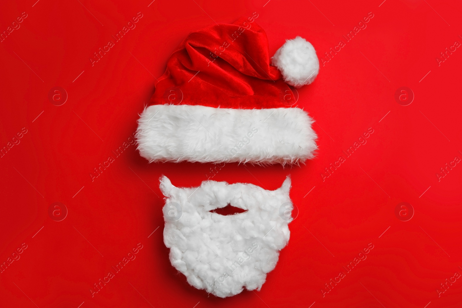 Photo of Santa Claus hat with white beard on red background, flat lay