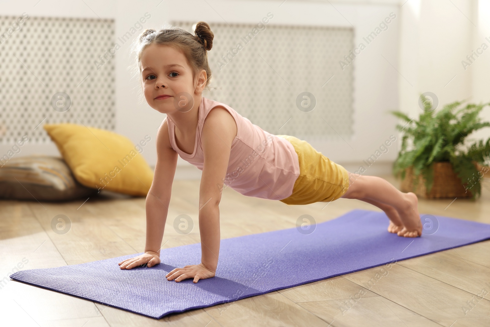 Photo of Little cute girl doing plank exercise on mat at home