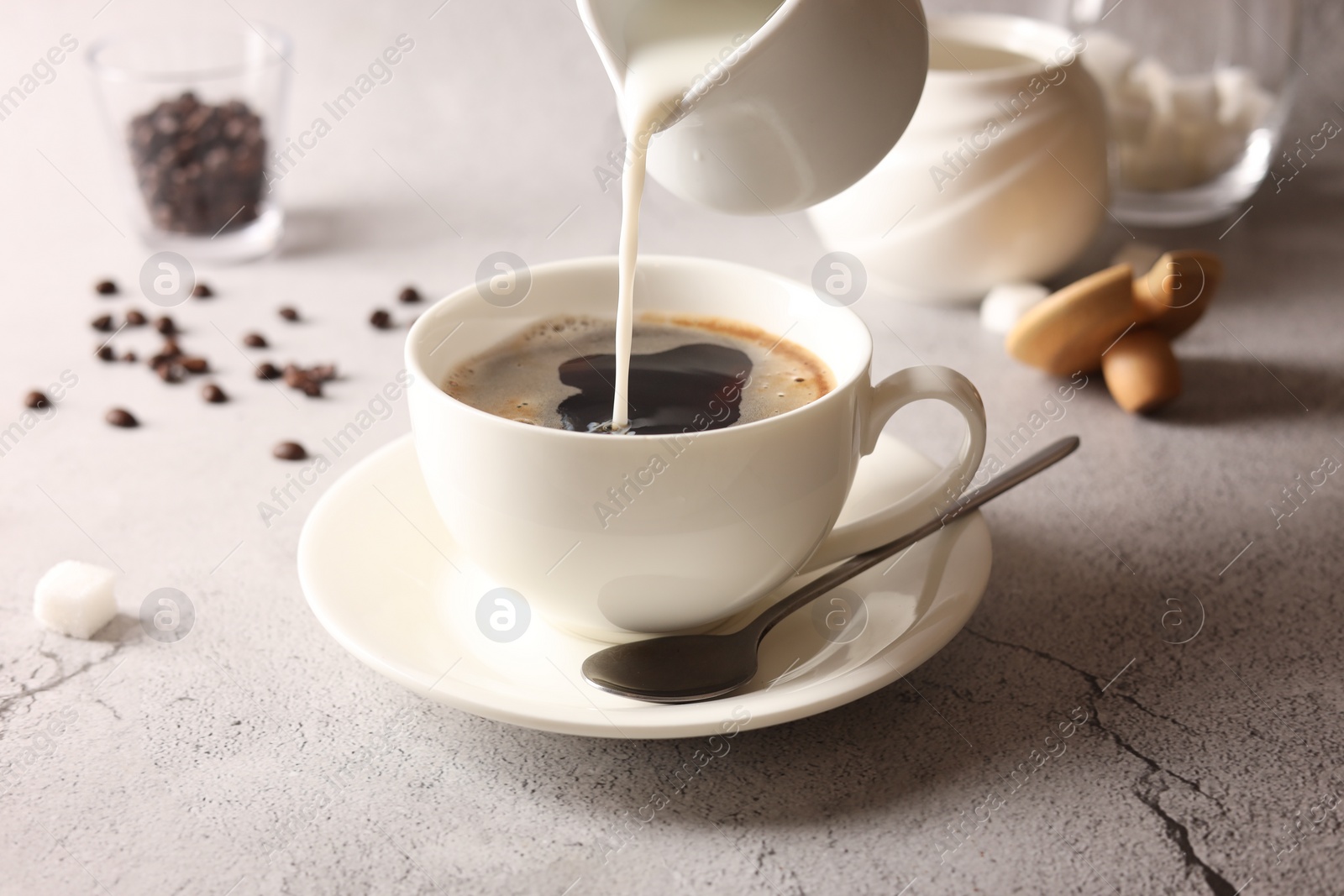 Photo of Pouring milk into cup with coffee on light grey textured table, closeup