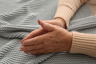 Photo of Elderly woman on grey knitted blanket, closeup