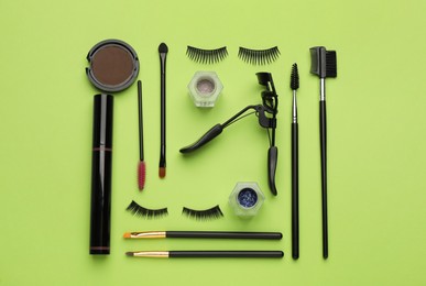 Photo of Flat lay composition with eyelash curler, makeup products and accessories on light green background