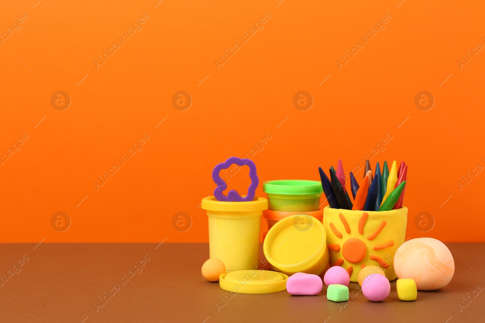 Photo of Set of bright play dough with mold and pencils on color background. Space for text