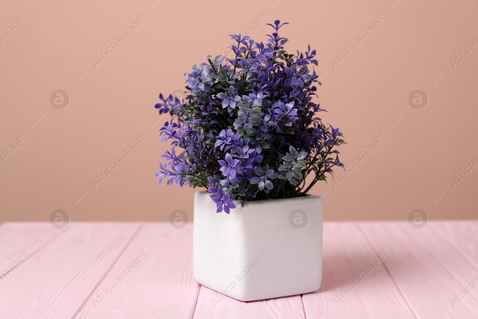 Photo of Purple artificial plant in white flower pot on pink wooden table