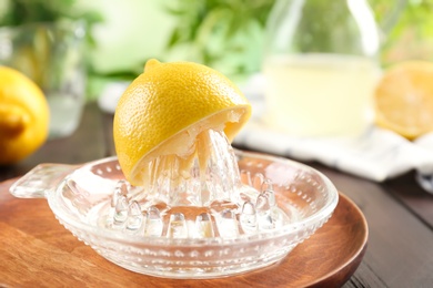 Glass citrus squeezer with lemon half on wooden plate