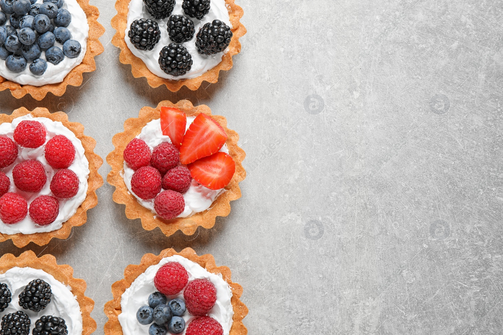 Photo of Many different berry tarts on table, flat lay with space for text. Delicious pastries