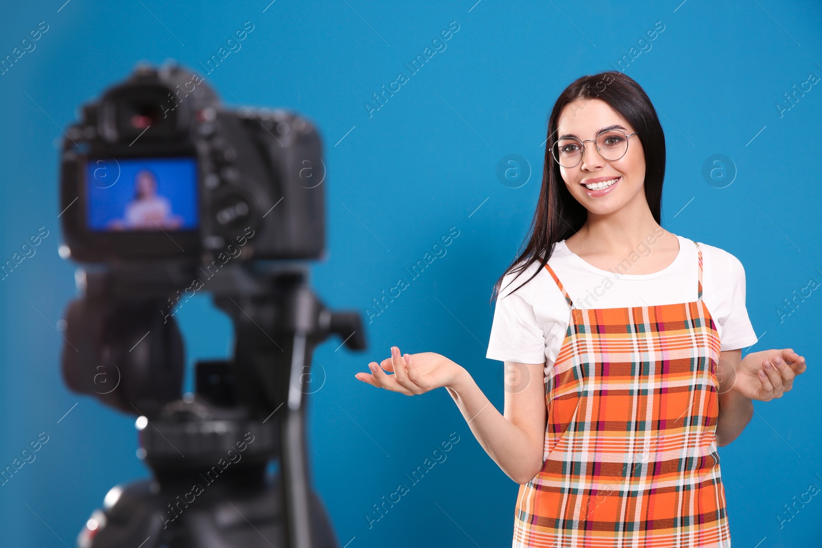 Photo of Young blogger recording video on camera against blue background