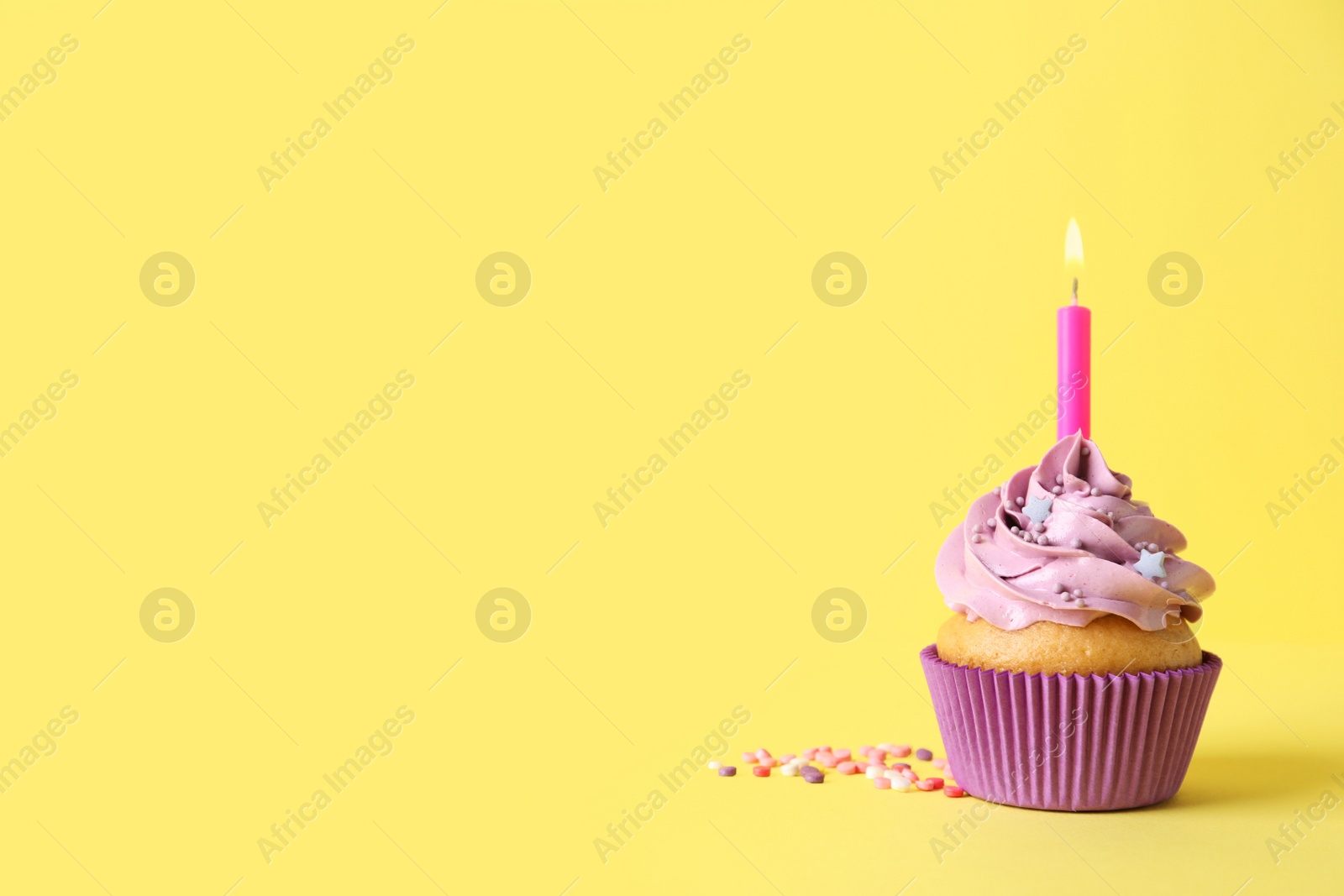 Photo of Birthday cupcake with burning candle and sprinkles on yellow background. space for text