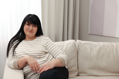 Photo of Beautiful overweight woman sitting on sofa at home