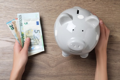 Photo of Woman with piggy bank and Euro banknotes at wooden table, top view. Money savings