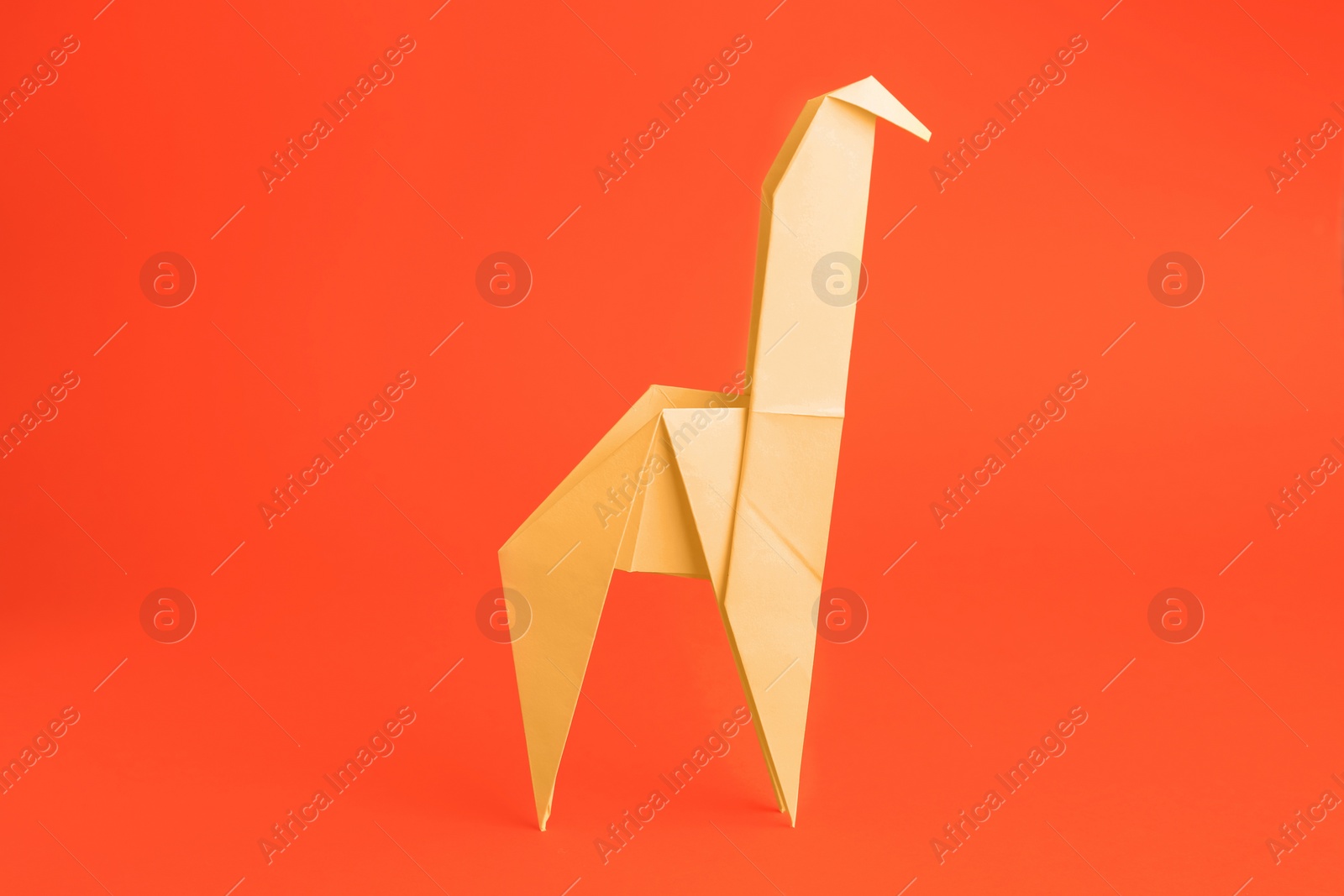 Photo of Origami art. Handmade yellow paper giraffe on orange background