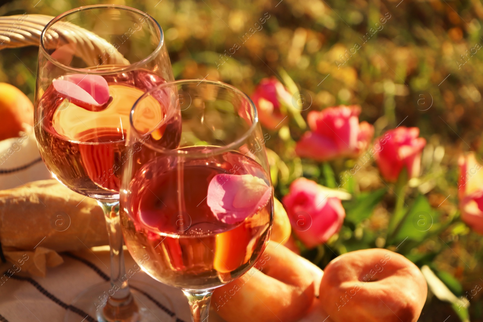 Photo of Glasses of delicious rose wine with petals outside. Space for text