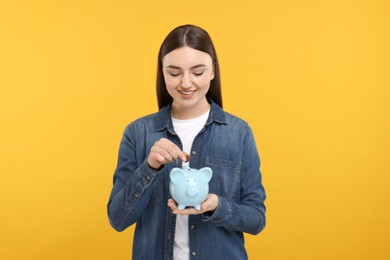 Photo of Happy woman putting coin into piggy bank on orange background