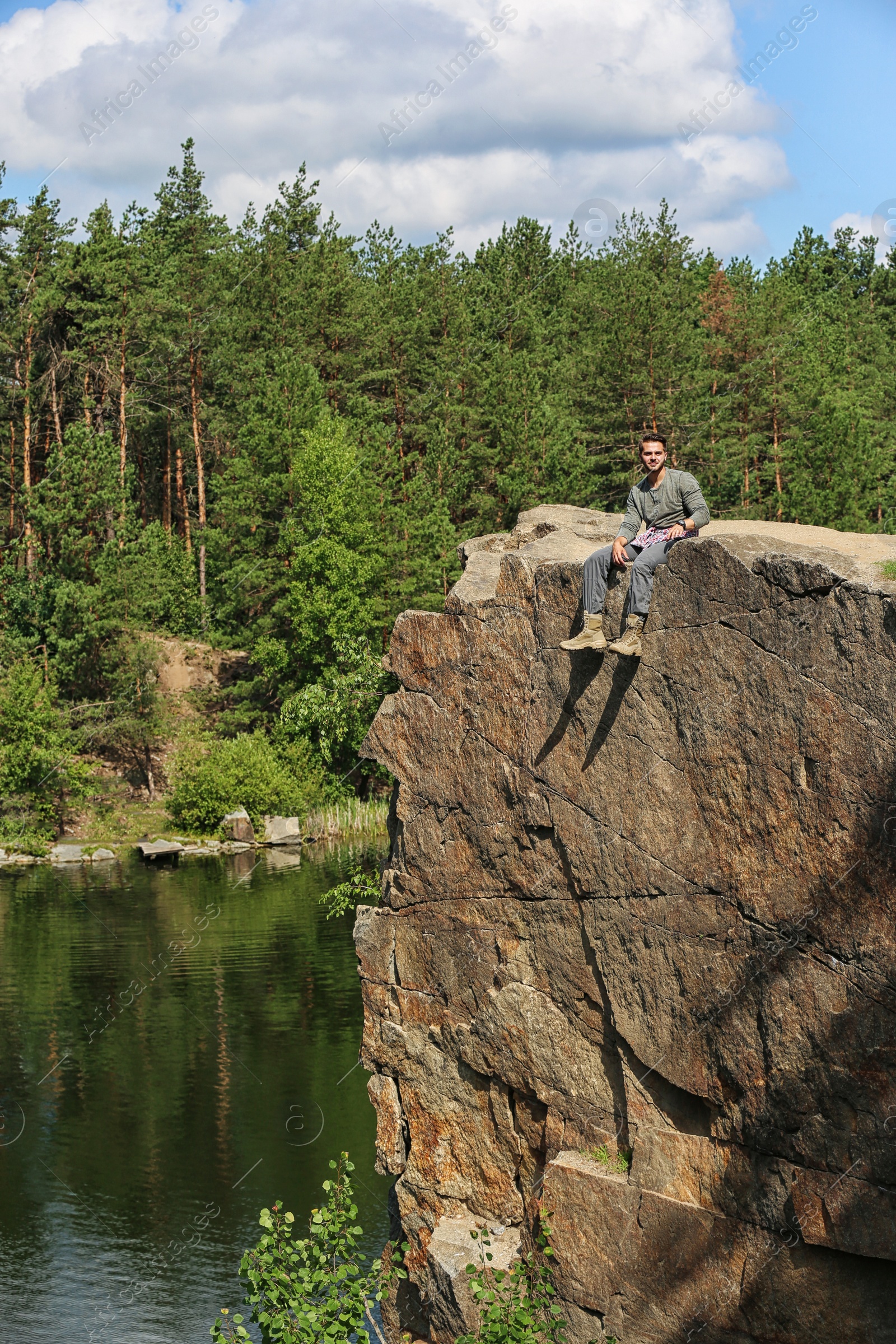 Photo of Young man on rock near lake and forest. Camping season