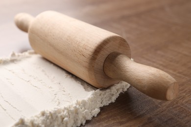 Photo of Flour and rolling pin on wooden table, closeup